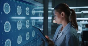 Caucasian Female Medical Researcher Analyzes MRI Brain Scans on Wall Display While Working on Digital Tablet Inside an Advanced Biotech Laboratory for Neuroscience Treatment. - Powered by Shutterstock - Get 15% off with code: PIKWIZARD15