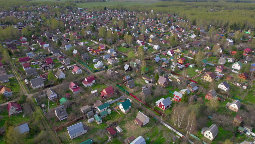 Low drone view passes over country houses gardens and roads with forest behind the village for rural lifestyle residential real estate and spring countryside themes
