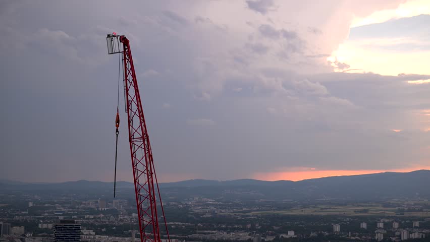 Tall red construction crane stands above the Frankfurt cityscape as storm clouds and sunset light meet on the horizon.