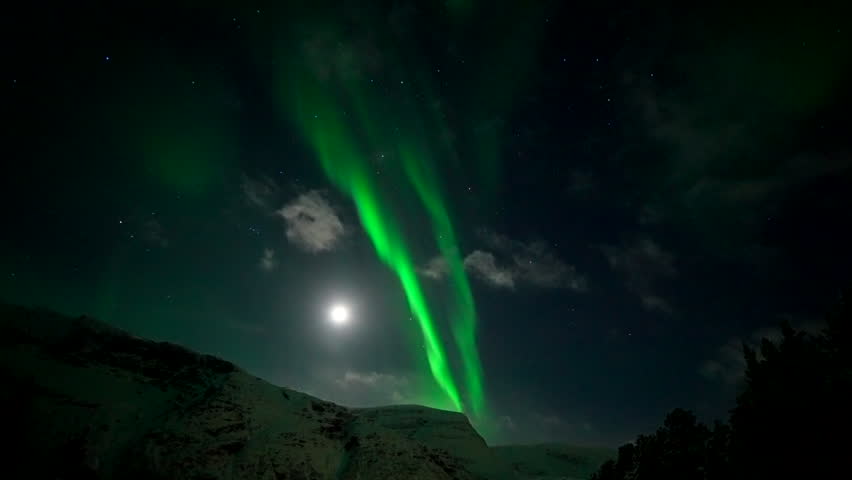 Magical green aurora borealis dance over snowy mountain at night with full moon