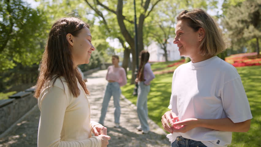 Caring mother talking with her adult daughter while standing in a sunny park. Two generations sharing a special moment of communication