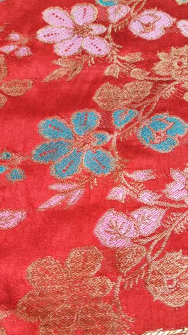 Luxurious red brocade or songket fabric gently flowing and rippling. Intricate gold, pink, and turquoise floral patterns shimmer as the silk satin material moves. Elegant texture for wedding, Lunar New Year, luxury fashion and oriental concept background.