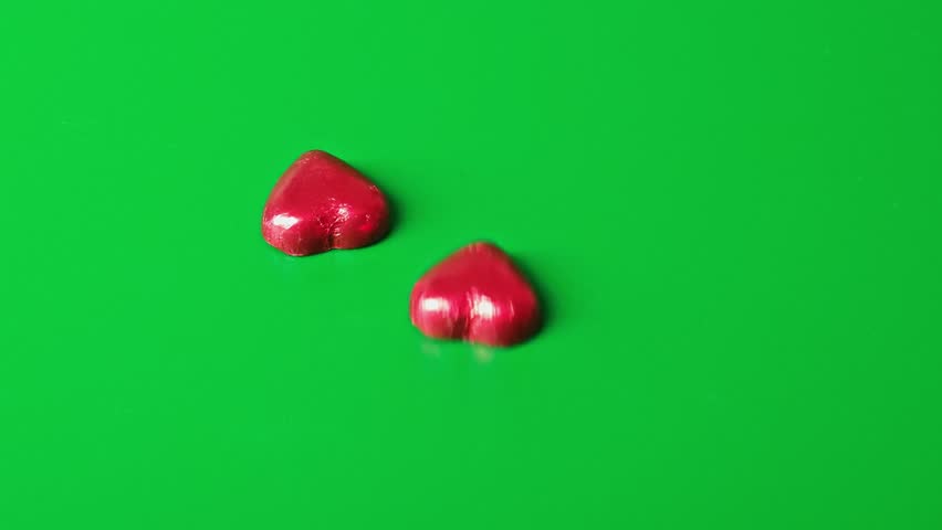 Group of small red heart shapes on a green surface being arranged and displayed