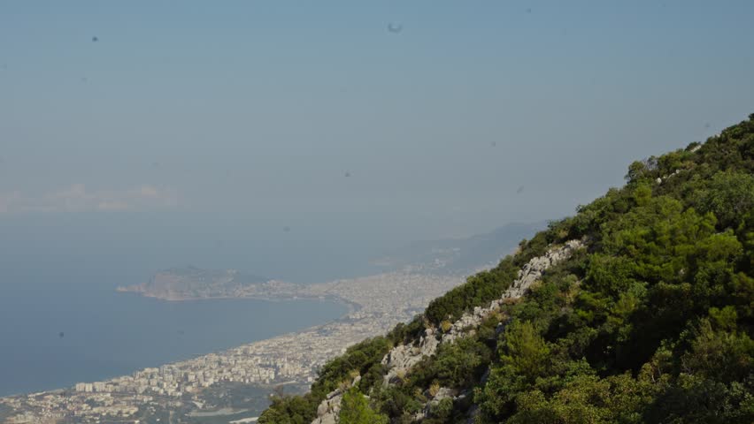 Wide shot of a coastline with green hills and blue ocean under a clear sky.