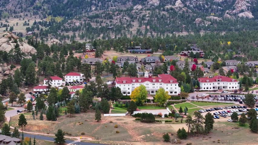 Panoramic cinematic aerial view of historic Stanley Hotel in Estes Park, Colorado town with fall foliage colors and surrounding cabins and mountain landscapes during the autumn season - 4K Drone