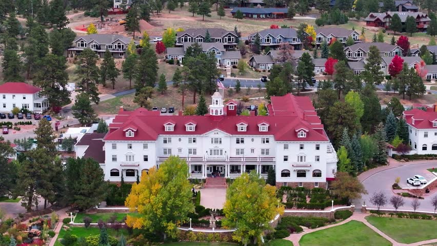 Cinematic aerial view of historic Stanley Hotel in Estes Park, Colorado town with fall foliage colors and surrounding cabins and mountain landscapes during the autumn season - 4K Drone