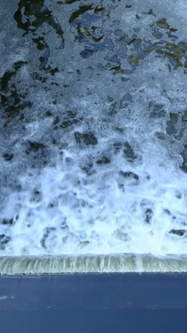 River water cascading over concrete spillway edge with foam.