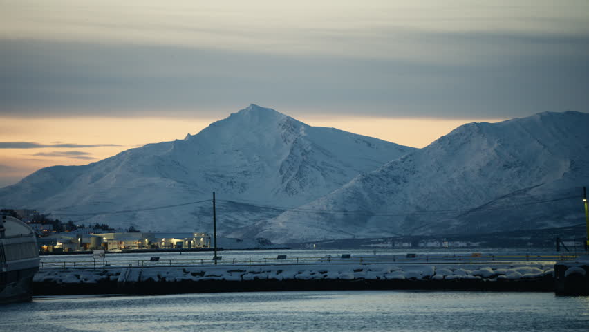 Snow covered Arctic mountain range beyond harbor waters under muted winter light