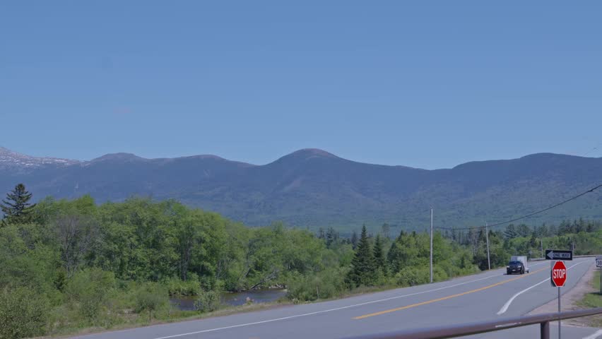Car with trailer driving past Presidential Mountain Range along scenic highway in White Mountain National Forest, New Hampshire