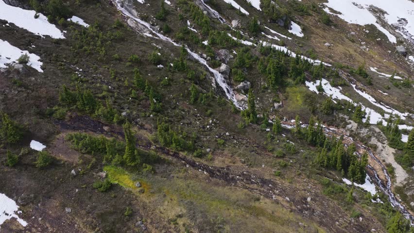 Stunning Waterfall Cascading Down a Verdant Mountain Slope with Patches of Snow in British Columbia, Canada