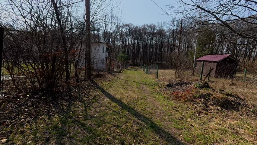 A drive along a dirt road leading to a country house. It captures the arrival and views of the rural landscape and open area nearby.