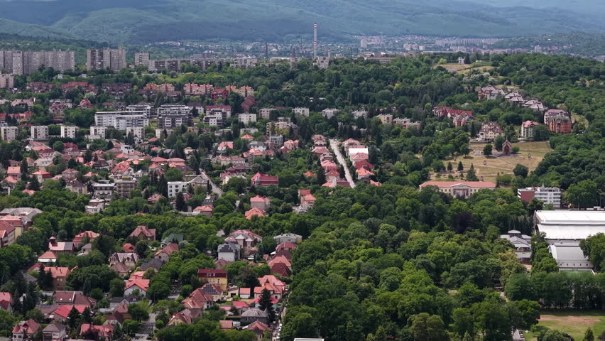 A high-angle view of the Hungarian city of Miskolc, showing a dense residential area surrounded by vibrant green forested hills.
