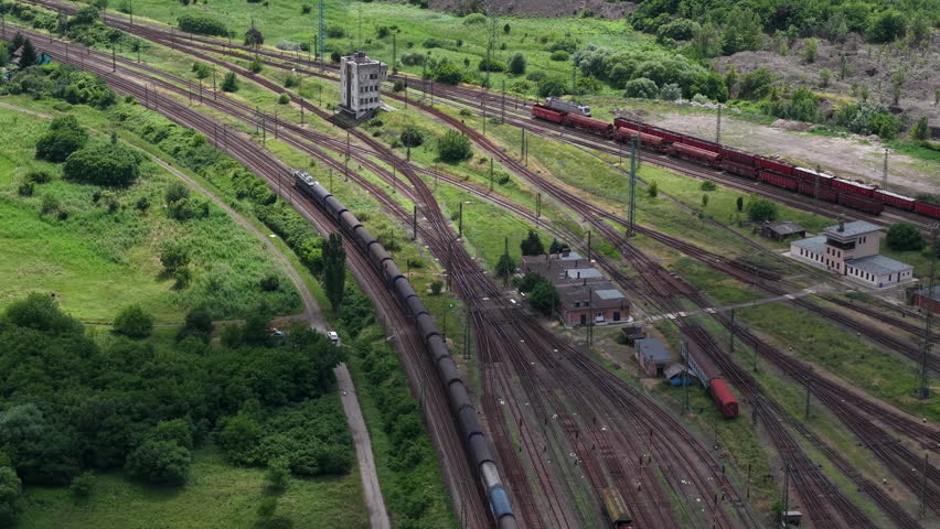 An aerial high angle view captures multiple freight trains and cargo wagons moving through a large industrial railway junction.