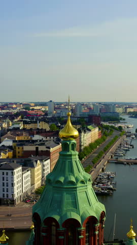 Vertical video. Helsinki, Finland. Uspenski Cathedral dominates the Katajanokka peninsula skyline with its distinctive red-brick facade and green copper domes crowned by gilded onion cupolas. The aerial view captures the cathedral