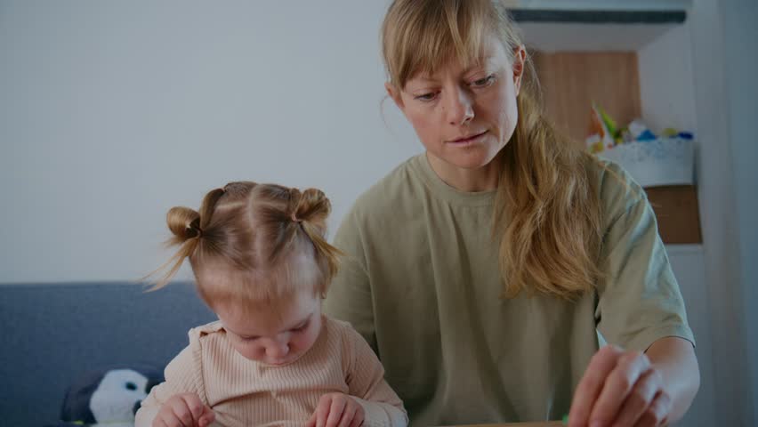 Mother and toddler work on a puzzle together. The child is focused, hands busy, eyes intent. The mother guides gently, expression calm and patient. Both seem relaxed, enjoying quiet time