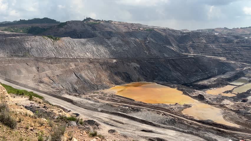 Landscape footage showing the vast scale of the open-pit coal mine, including large yellowish acid mine drainage ponds.