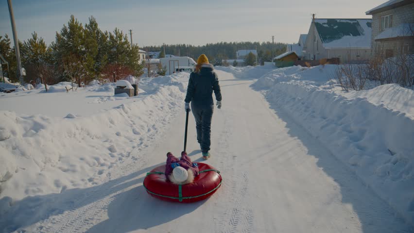 Person pulls red sled with child down snow-covered street. Clear winter sky above quiet neighborhood. Bright red sled contrasts white snow. Perfect for holiday or winter family scenes
