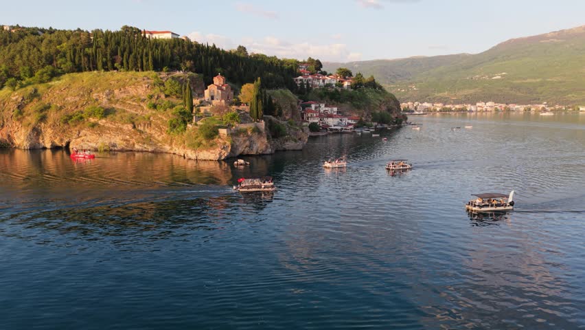 Several tourist boats sail near the shore by Church of St. John at Kaneo on Lake Ohrid.