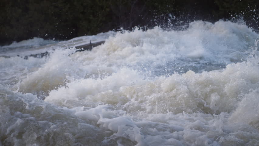 Spring water crashes over a concrete weir structure at Sauble Falls, Ontario. The high-speed capture details the explosive power of the crashing waves and flying water droplets.