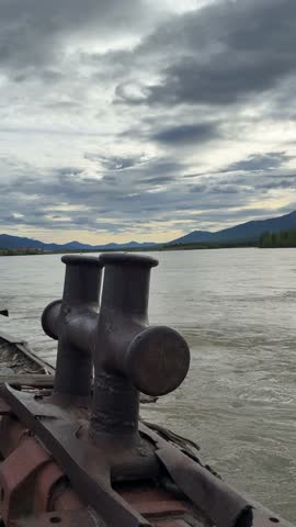 A boat cleat on a vessel with a river, mountains, and cloudy sky in Ust-Nera, Russia