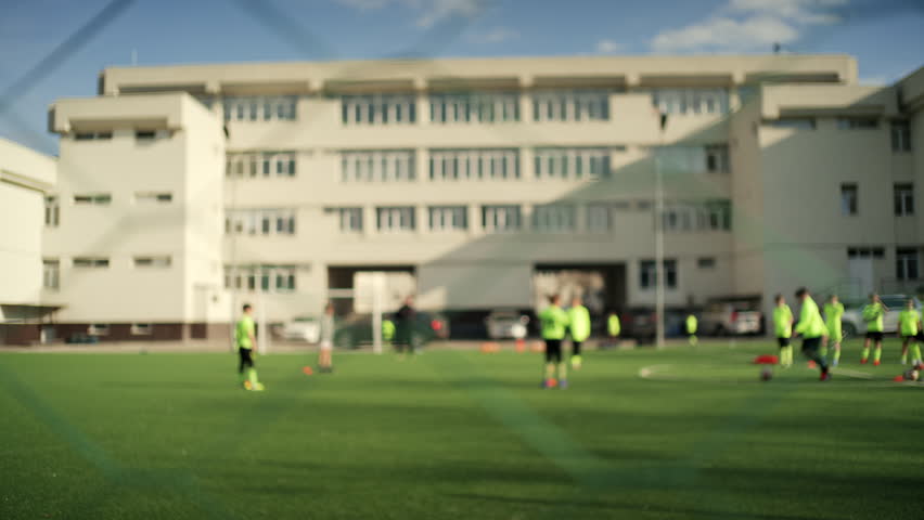 Blurred shot of a youth football training session on an outdoor artificial turf field near a school building