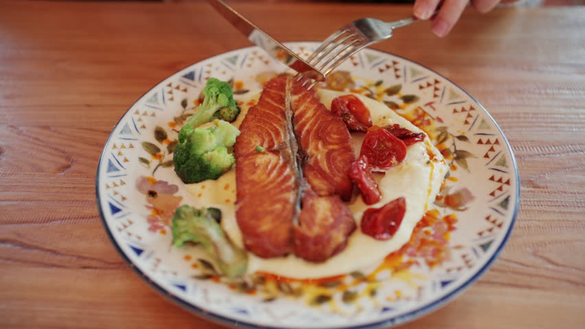Close up of grilled salmon fillet served with creamy mashed potatoes, roasted cherry tomatoes, and broccoli