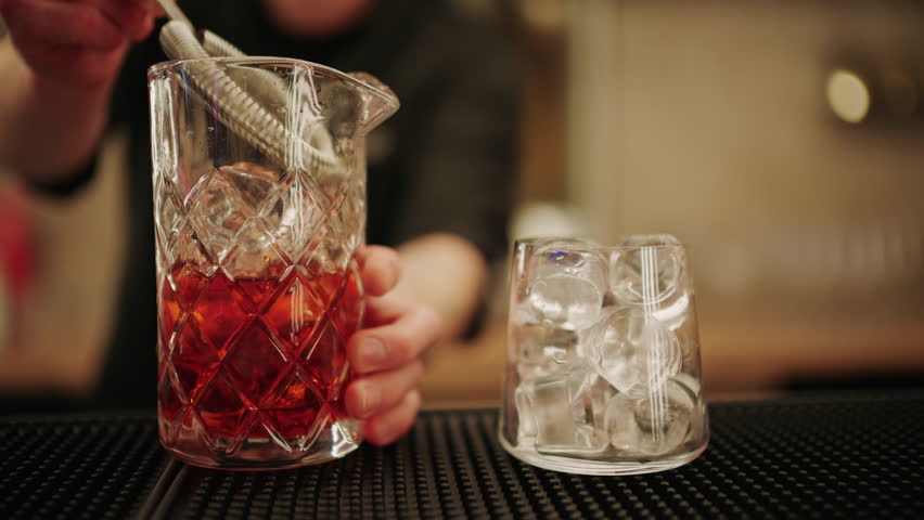 Bartender pouring a freshly mixed red cocktail into a glass filled with ice