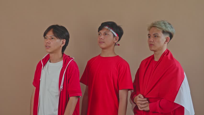 Three Indonesian teenagers standing in row and saluting respectably for Independence Day in studio