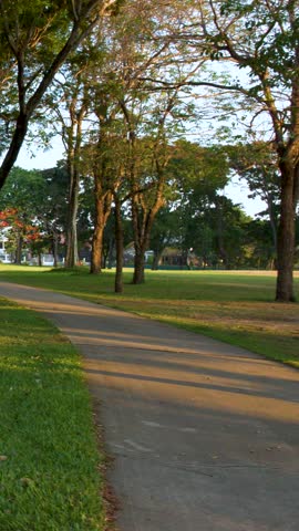 A smooth camera pan follows a curved walkway through lush green grass and tall trees.