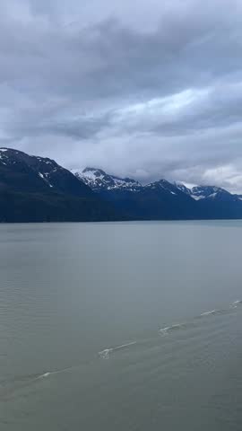 Wide Fjord with Snowy Mountains and Dramatic Clouds in Alaska

Wide shot of a large fjord with calm gray water and boat wake, surrounded by majestic snow covered mountains under dramatic cloudy sky in Alaska. Epic coastal landscape for nature, travel and documentary footage.