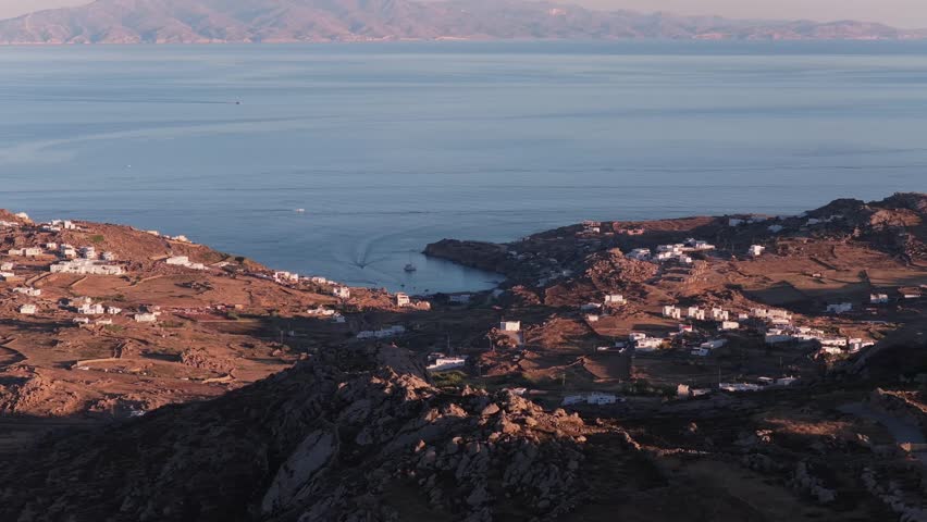 Rocky coastline of Mykonos with traditional whitewashed houses in Aegean Sea at sunset revealing a telecommunication tower in Greece