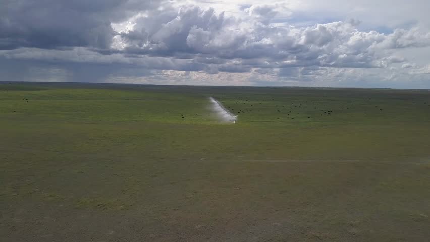 Flyover expansive prairie pasture with irrigation pivot under cloud sky