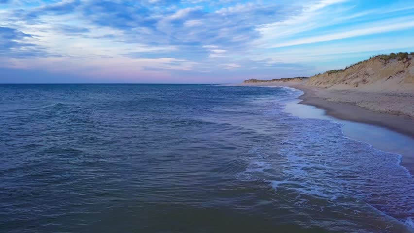 Sandy shoreline and calm blue sea beside coastal dunes