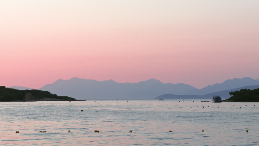 Sunset over the Albanian Riviera with calm sea and mountain silhouette
