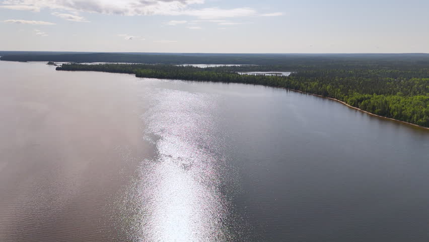 Drone flight facing the sun across the vast waters of Nagagamisis Lake, where glittering reflections lead toward the distant boreal forest of Northern Ontario.