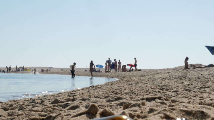 Summer Beach Scene With People on Sandy Shoreline and Umbrellas Near Calm Ocean. Crowded summer beach with people and colorful umbrellas along a sandy shoreline, shallow calm water and bright clear sky conveying relaxation, leisure and warm vacation vibes.