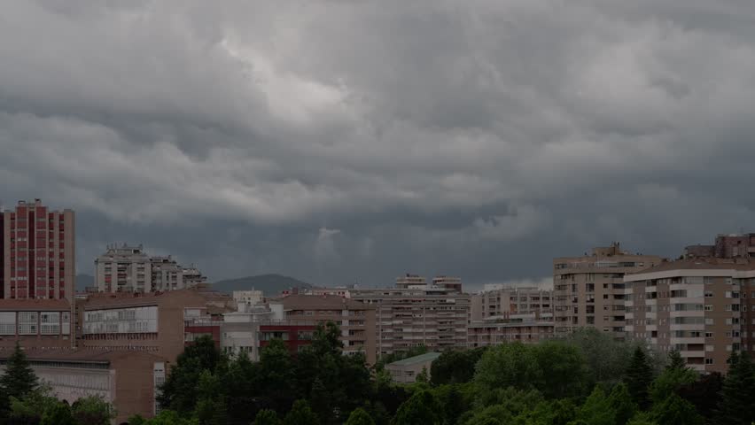A timelapse of overcast sky above urban buildings, with trees in the foreground in stormy rainy weather