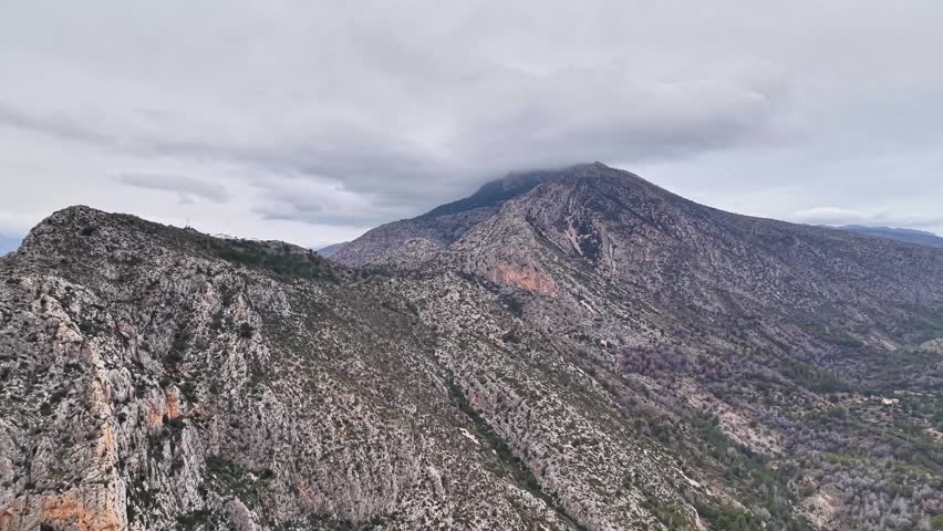 Aerial View Of Stormy Mountain Cliffs Expedition Flight Over Jagged Escarpments, Heavy Clouds Hugging Peak,