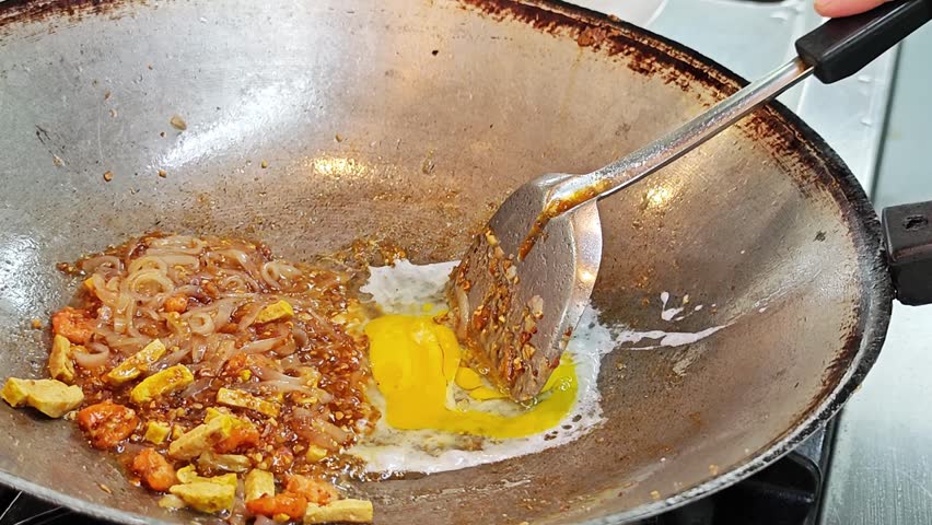 Scrambling an egg next to rice noodles in a wok close up.
