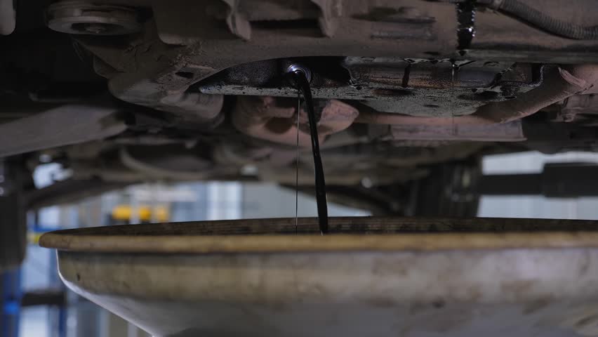 A detailed view of the car draining excess engine lubricant to ensure the required pressure during the engine oil change at the service station.