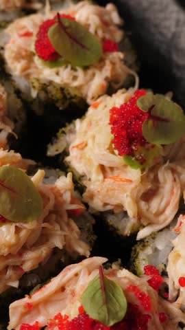 Sushi rolls with tobiko caviar on black platter, closeup. Japanese cuisine . Vertical footage