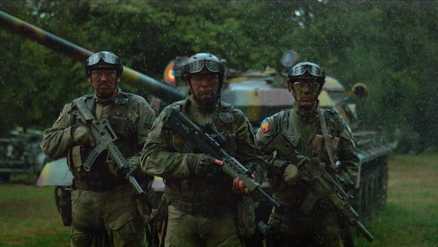 Three soldiers in tactical gear pose with rifles in heavy rain during an intense ultra slow motion training session.