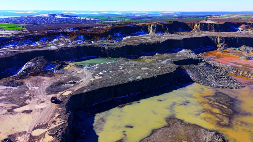 Panoramic view of quarry pit with mineral colored ponds. Green, yellow and orange water pools amid rock terraces and hills.