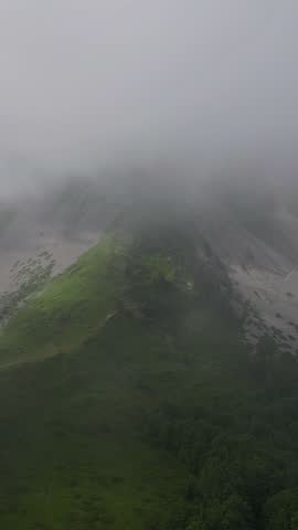 Thick morning fog and mist slowly drifting over a verdant mountain ridge. Mysterious and moody alpine landscape on a cloudy day