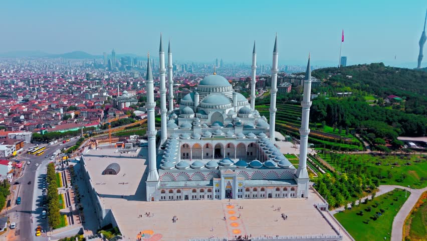 Aerial view of Grand Camlica Mosque in Istanbul. White domes, tall minarets, landscaped grounds and urban buildings form a striking city panorama.