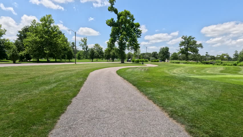 POV Walking on Recreational Public Park Trail. A smooth first-person view moving down a curved pedestrian walking path lined by beautiful manicured lawns and mature trees in Forest Park, St. Louis, Missouri.