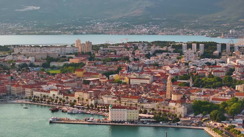Split shows a coastal city with a mix of historical and modern buildings. The waterfront area features boats and green spaces. Mountains are visible in the background.