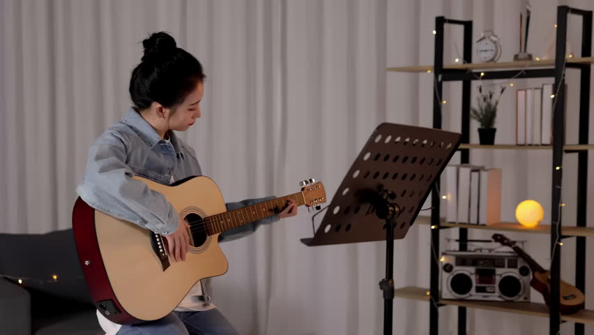 Girl musician looks at note for guitar on music stand, practicing playing acoustic guitar. Music teacher reviews new material at sheet music in front of her while selecting chords, play instrument