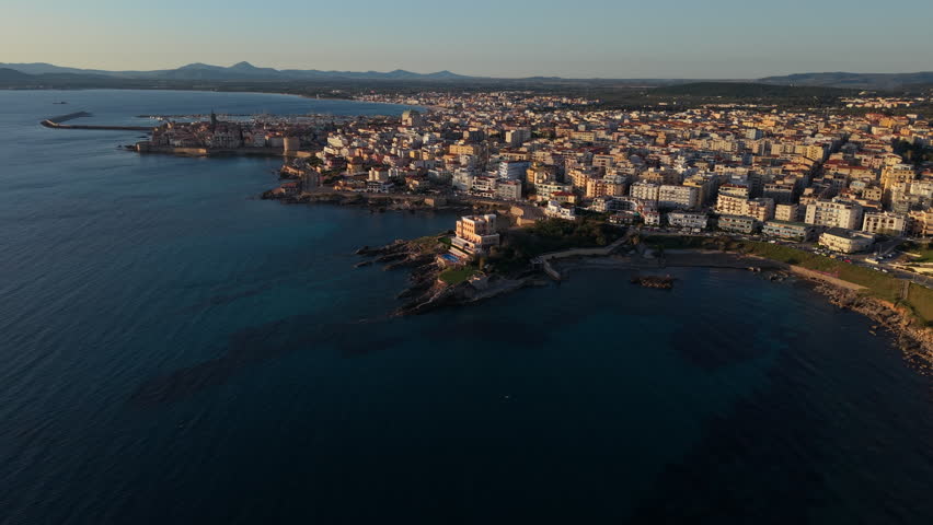 Historic Coastal Town Of Alghero By Turquoise Sea At Sunrise In Sardinia. - aerial shot