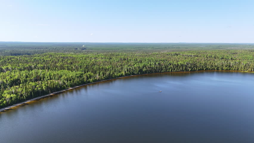 Drone view of Nagagamisis Lake showcasing a long sandy shoreline, a small boat, and vast boreal forest stretching to the horizon in Northern Ontario.